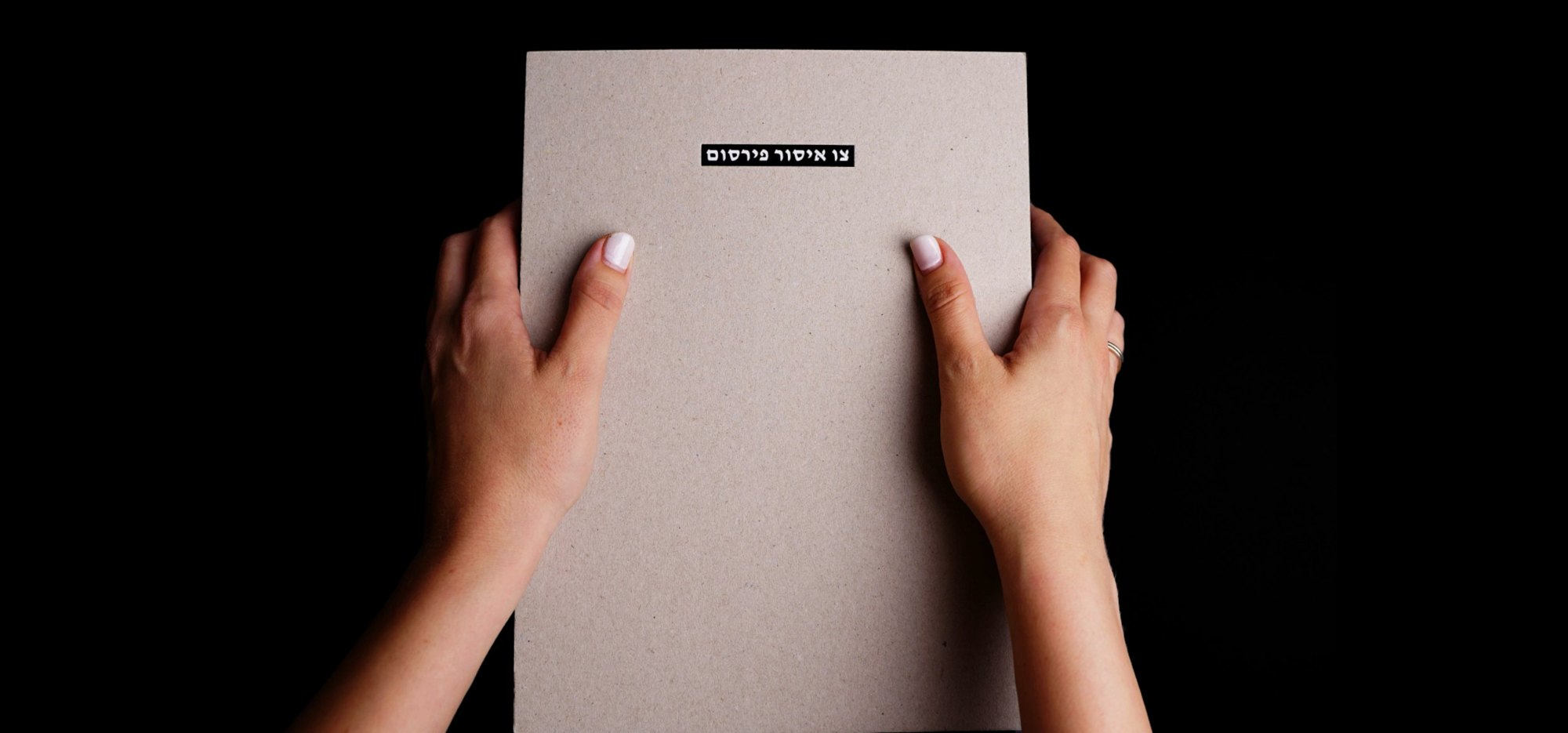 Hands holding Tzav Issur Pirsum, a grey cardboard book with a black label